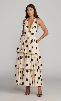 A woman wearing the Mac Duggal 27833 long formal dress in black ivory—a halter neck style with large black polka dots—and black high-heeled sandals, standing against a plain gray background.