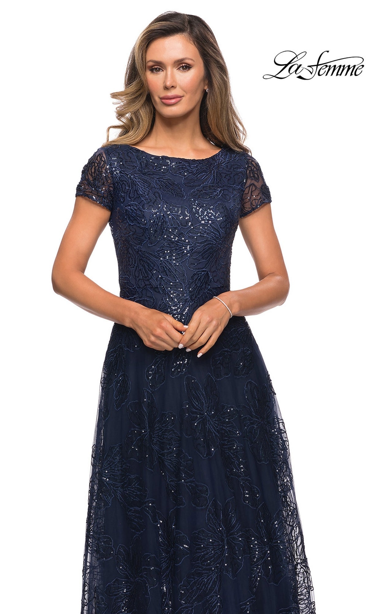 A woman wears a La Femme 27837 navy blue floor-length evening gown with short sleeves, floral embroidery, and sequin lace details.
