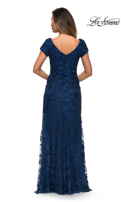 Woman wearing Long Formal Dress: La Femme 27842—navy floor-length, short-sleeve lace with floral details and sheath skirt, shown from the back. “La Femme” logo upper right.