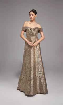 A woman poses against a plain gray background wearing the Alyce 27844 long formal dress in cappuccino, an off-the-shoulder jacquard gown with a leaf-like metallic pattern—ideal as a mother-of-the-bride ensemble.