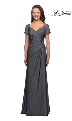Woman in a floor-length, short-sleeved A-line Long Formal Dress: La Femme 27855 in gunmetal with V-neck and gathered waist, smiling by a white background. “La Femme” logo top right.