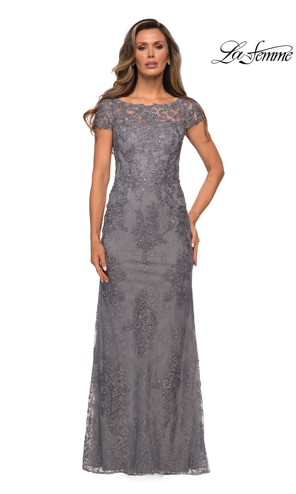 A woman wearing a dark platinum Long Formal Dress: La Femme 27856, a dark gray lace floor-length sheath with cap sleeves, floral embroidery, and a sheer neckline.