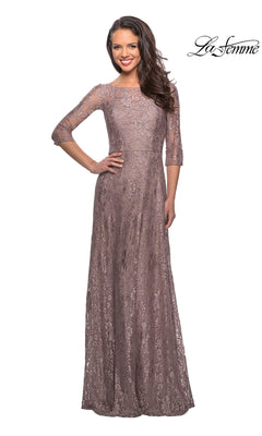 A woman wearing a cocoa-colored La Femme 27857 long formal dress featuring floor-length lace, three-quarter sleeves, and a high illusion neckline.