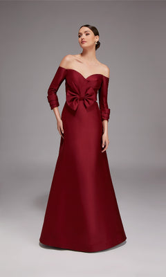 A woman wearing the Alyce 27859 long formal dress in burgundy with three-quarter sleeves and a large waist bow stands against a plain gray background.