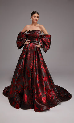 A woman stands against a plain gray background wearing the Alyce 27862 long formal dress in black/red, featuring an off-the-shoulder design, floor-length floral jacquard fabric, voluminous sleeves, and red floral patterns on a dark base.
