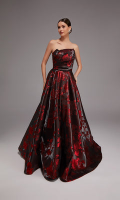 A woman stands against a plain gray background wearing the Alyce 27862 long formal strapless black jacquard dress with a red floral pattern.