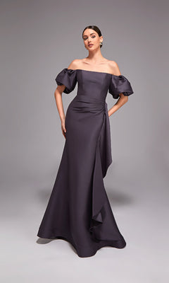 A woman poses in the Alyce 27863 long formal dress—an off-the-shoulder style with puff sleeves, a draped waist, and a fitted silhouette—against a plain gray background.