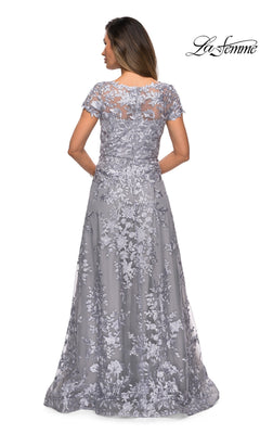 Woman in a silver-gray floor-length gown with short sleeves and a floral lace overlay, shown from the back. The Long Formal Dress: La Femme 27870 offers a graceful silhouette, making it an elegant choice for special occasions such as mother of the bride events.