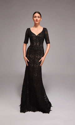 A woman poses in a studio wearing the Alyce 27871—a long formal dress featuring a fitted black lace overlay, short sleeves, and a V-neckline.