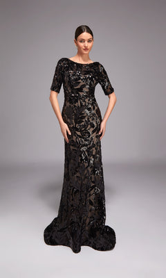 A woman poses against a plain gray background wearing the Alyce 27876 long formal dress—a floor-length black gown with short sleeves, sheer accents, and sequin floral detailing.