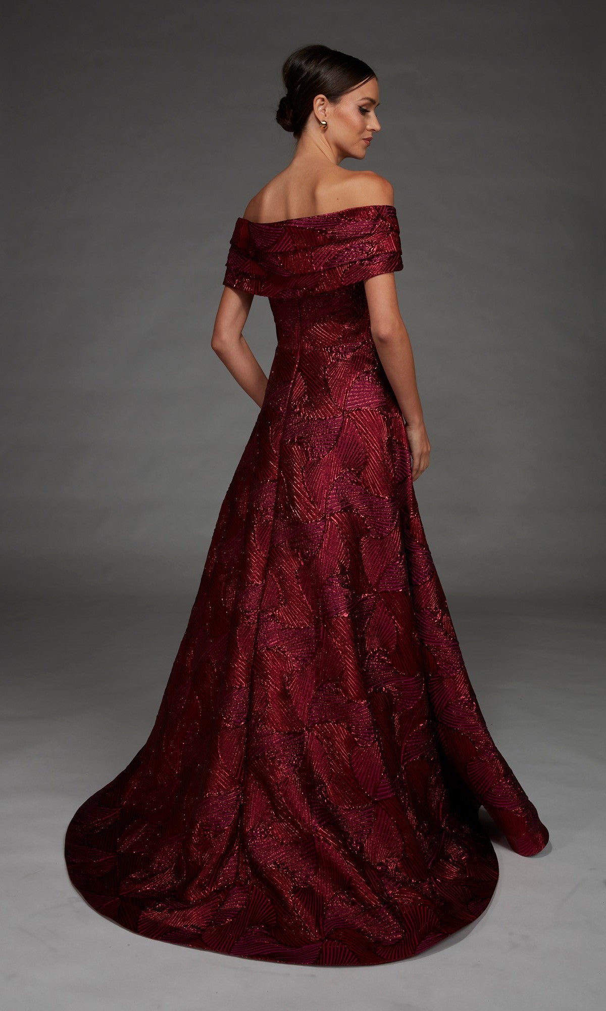 A woman wearing the Alyce 27884 long formal dress—an off-the-shoulder, floor-length, dark red jacquard gown featuring a textured leaf pattern and an elegant A-line skirt—stands against a plain gray background.
