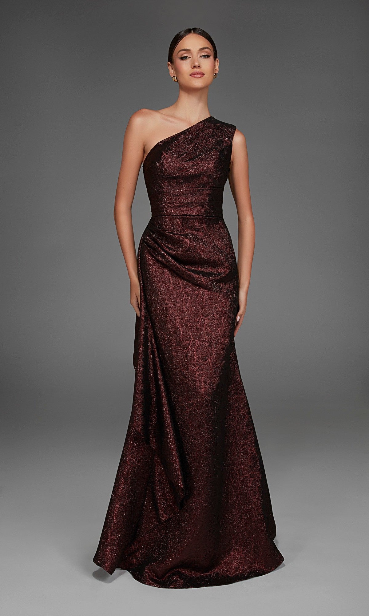A woman wearing the Alyce 27885 long formal dress in Black Cherry, featuring a one-shoulder design and subtle pattern, poses against a plain gray background.