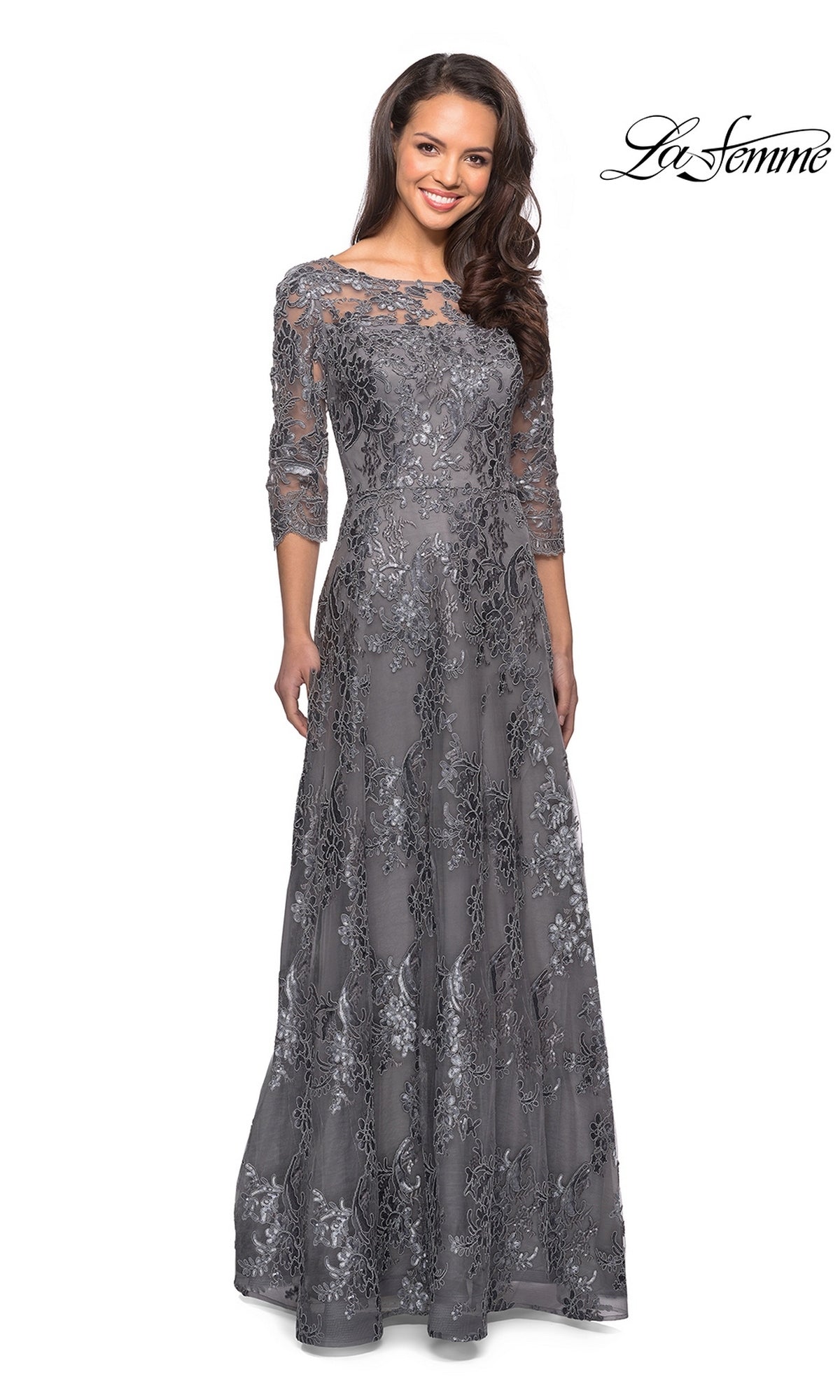 A woman wears a platinum Long Formal Dress: La Femme 27885, a long, gray sequin-lace formal dress with three-quarter sleeves and floral embroidery.