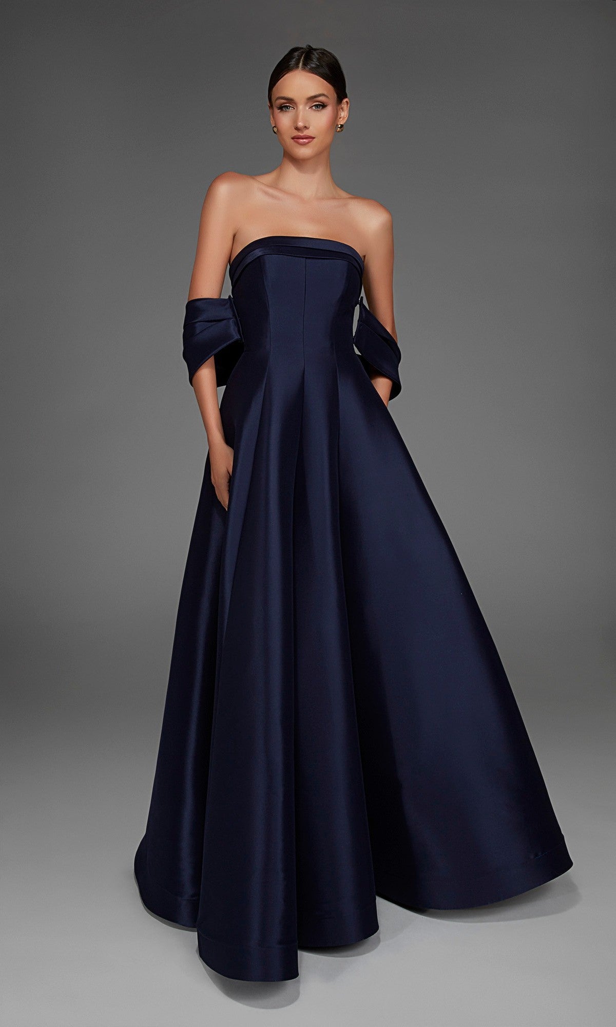 A woman wearing the Alyce 27887 long formal dress in midnight, featuring a strapless design with off-the-shoulder sleeves, stands against a plain gray background.