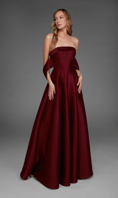 A woman wearing the Alyce 27887 long formal dress in burgundy, featuring a strapless, floor-length design with a fitted bodice and draped fabric at the arms, stands against a plain gray background.
