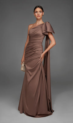 A woman stands against a plain gray background wearing the Alyce 27891 long formal dress in Shadow Grey, a floor-length, one-shoulder satin evening gown featuring a dramatic bow detail. She holds a small gold clutch, making an elegant statement in this figure-flattering formal look.
