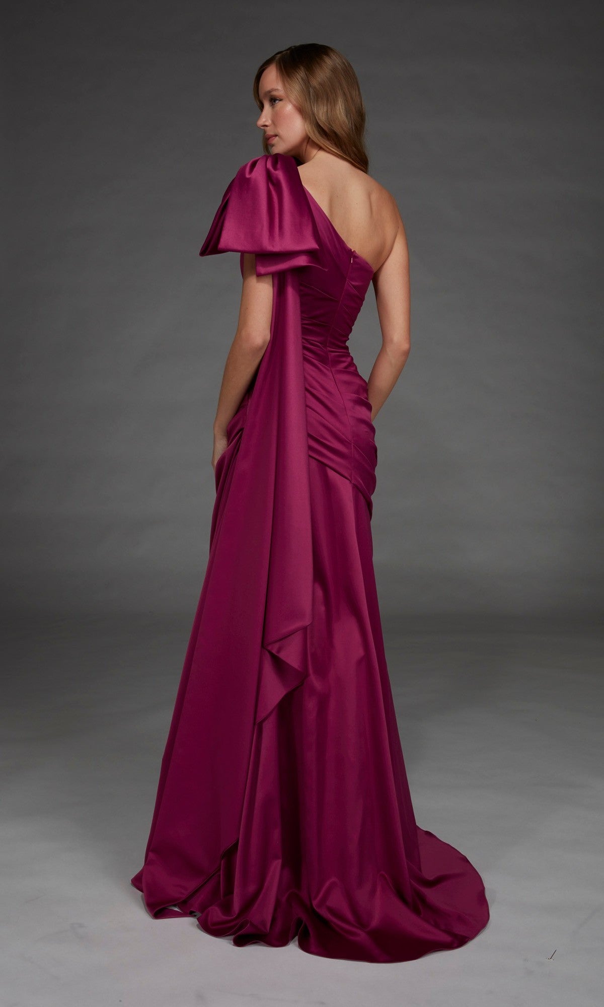 A woman wearing the Long Formal Dress: Alyce 27891—a magenta, one-shoulder satin evening gown with draped fabric detail—stands against a gray background.