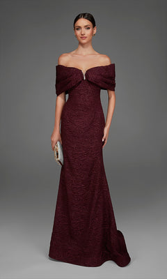 A woman wearing the Long Formal Dress: Alyce 27894 in Black Cherry, featuring an off-the-shoulder, floor-length mermaid silhouette with textured rose-patterned brocade, holds a small metallic clutch and stands against a plain gray background.