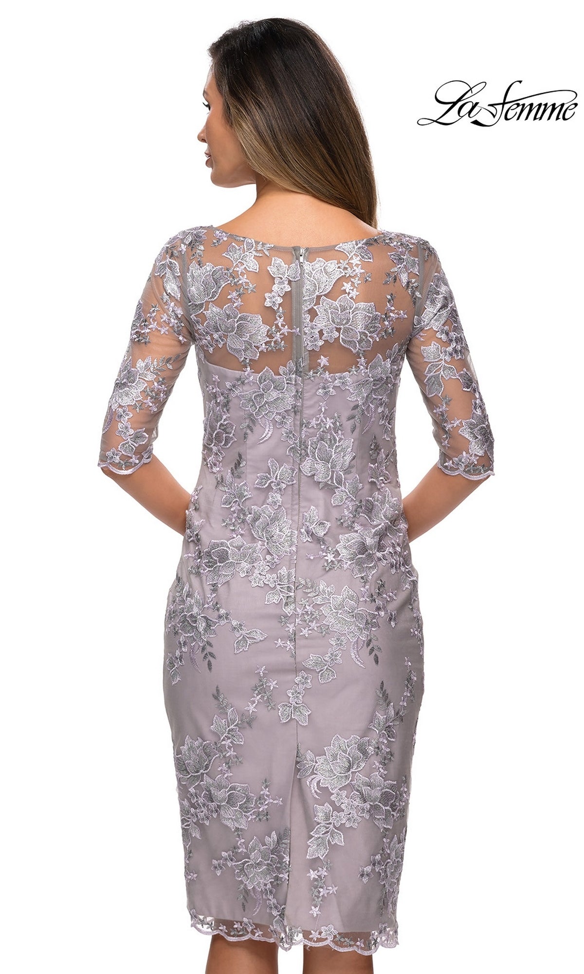 Woman facing away, wearing the Knee Length Wedding Guest Dress: La Femme 27895 in light purple floral lace with sheer half sleeves. “La Femme” logo in top right corner.