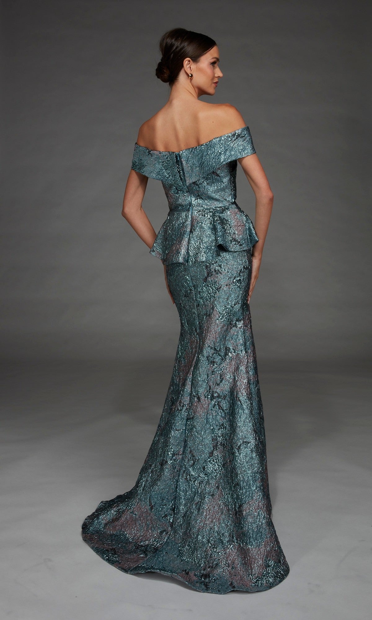 A woman wearing the Long Formal Dress: Alyce 27899, which features an off-the-shoulder neckline and a structured peplum waist, crafted from textured metallic teal fabric, stands in a studio with a plain gray background.