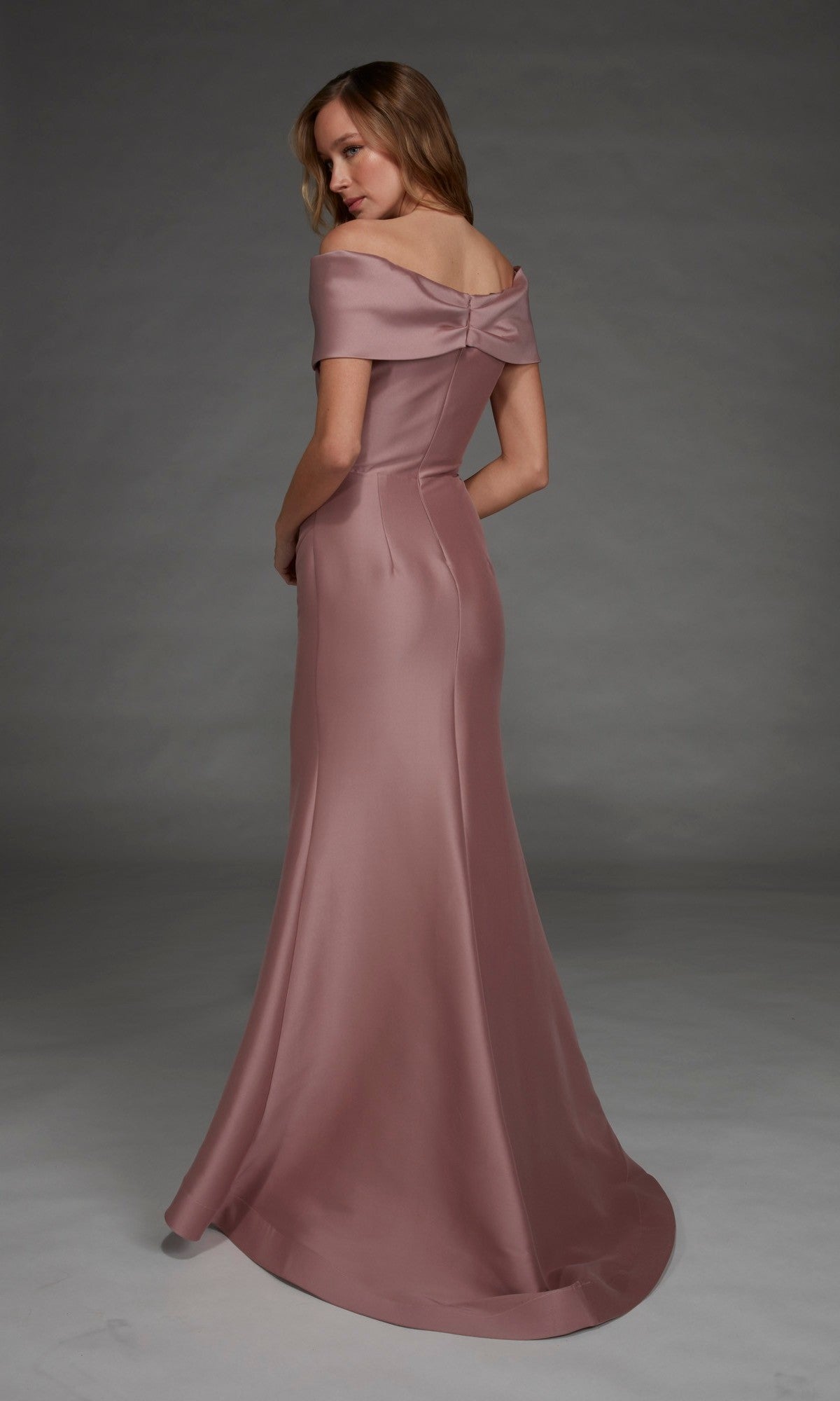 A woman stands against a plain gray background wearing the Long Formal Dress: Alyce 27908, a floor-length gown in mauve satin stretch mikado featuring off-the-shoulder sleeves and a bow detail on the back.