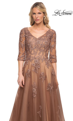 A woman wears the Long Formal Dress: La Femme 27908, a brown lace V-neck evening gown with elbow-length sleeves, floral embroidery, and a full skirt.