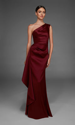 A woman wearing the Alyce 27913 long formal dress in burgundy, featuring a floor-length satin design with draped detailing and an elegant one-shoulder neckline, stands against a plain gray background.