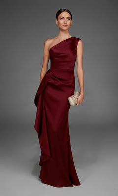 A woman wearing the Alyce 27913 long formal dress—a burgundy satin evening gown featuring an elegant one-shoulder neckline and draped detailing—holds a small metallic clutch while standing against a plain gray background.