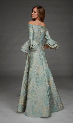 A woman models the Long Formal Dress: Alyce 27914, an off-the-shoulder evening gown crafted from textured light blue fabric with flared sleeves and a graceful A-line silhouette; she stands in a studio setting facing away from the camera.