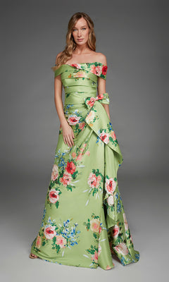 A woman wearing the Alyce 27915 long formal dress in peridot green, featuring an off-the-shoulder design and embellished with red and blue floral accents, stands against a plain gray background.