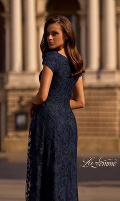 A woman wearing the Long Formal Dress: La Femme 27915 poses outside a classical stone building, looking over her shoulder. The La Femme logo is visible in the lower right corner.