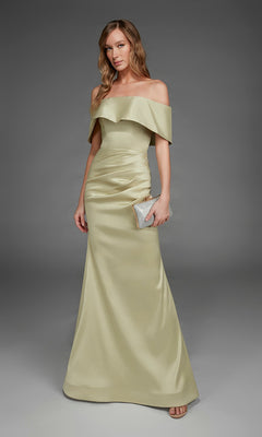 A woman wearing the Alyce 27916 long formal dress, an off-the-shoulder, floor-length gown in light gold stretch mikado satin, holds a silver clutch and stands against a plain gray background.