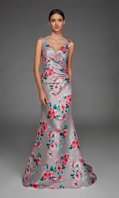 A woman wearing the Alyce 27917 Long Formal Dress—a floor-length, sleeveless, silver v-neck evening gown with a pink floral print—stands against a plain gray background.
