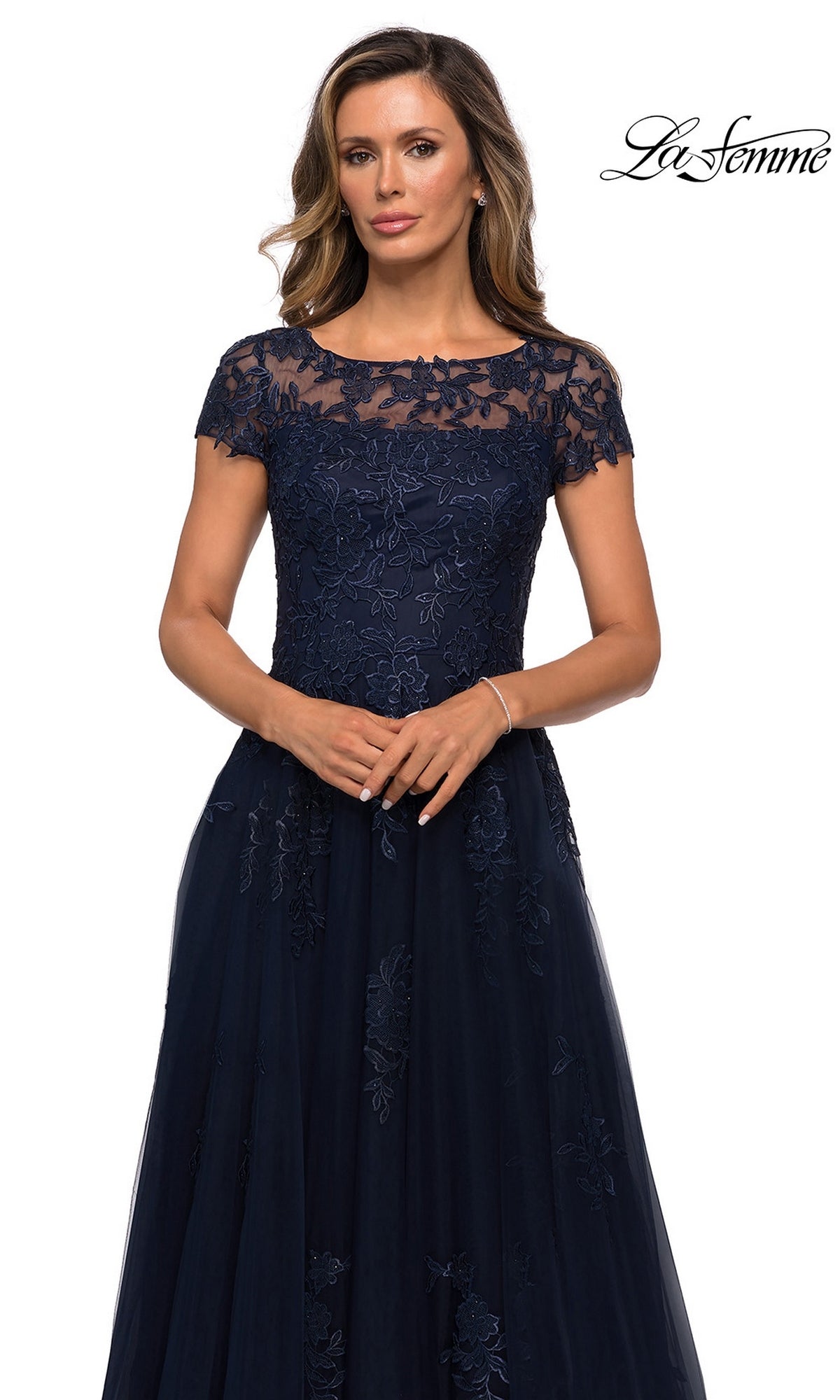 Woman wears Long Formal Dress: La Femme 27920, a navy blue floor-length gown with short sleeves and floral lace, against a white background.