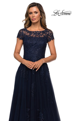 Woman wears Long Formal Dress: La Femme 27920, a navy blue floor-length gown with short sleeves and floral lace, against a white background.