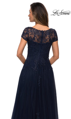 Woman facing away in a navy blue Long Formal Dress: La Femme 27920 with an A-line silhouette, short lace sleeves, and floral lace bodice. “La Femme” logo top right.