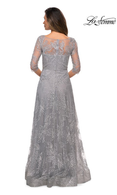 Woman facing away in Long Formal Dress: La Femme 27942—a floor-length silver sequined lace gown with three-quarter sleeves and sheer back. “La Femme” logo top right.