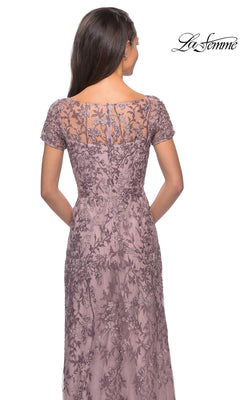 Woman in Long Formal Dress: La Femme 27956, lavender lace with short sleeves and floral beaded accents, seen from the back. “La Femme” logo top right.