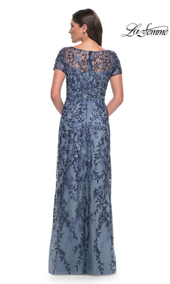 A woman stands with her back to the camera, wearing the Long Formal Dress: La Femme 27956, a blue lace evening gown with floral beaded details.