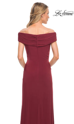 A woman in an off-the-shoulder, floor-length burgundy jersey gown, seen from behind with loose waves. “La Femme” logo appears top right. Product: Long Formal Dress: La Femme 27959.