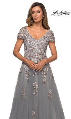 A woman wears a silver gray, short-sleeved La Femme 27968 formal dress with a V-neckline and floral embroidery extending from the bodice to the skirt.