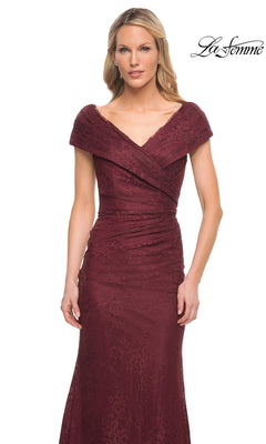 A woman wearing the La Femme 27982 long formal dress, featuring an off-the-shoulder design in burgundy lace with a fitted bodice and subtle floral pattern, stands against a white background.