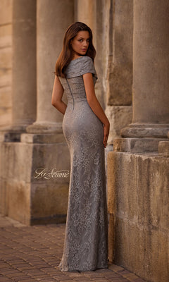 A woman wearing the La Femme 27982 long formal dress—a fitted gray lace gown with an off-the-shoulder, v-neckline—stands between stone columns, facing away while turning her head toward the camera.