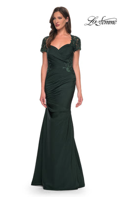 A woman wearing the La Femme 27989 long formal dress in dark emerald, featuring a floor-length satin-jersey design with short lace sleeves and a ruched bodice, stands against a plain white background.