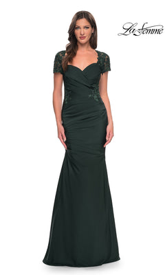 A woman stands against a white background wearing the La Femme 27989 long formal dress, featuring dark green satin-jersey fabric, a floor-length silhouette, short lace sleeves, a ruched bodice, and a sweetheart neckline. The word “La Femme” appears in the top right.