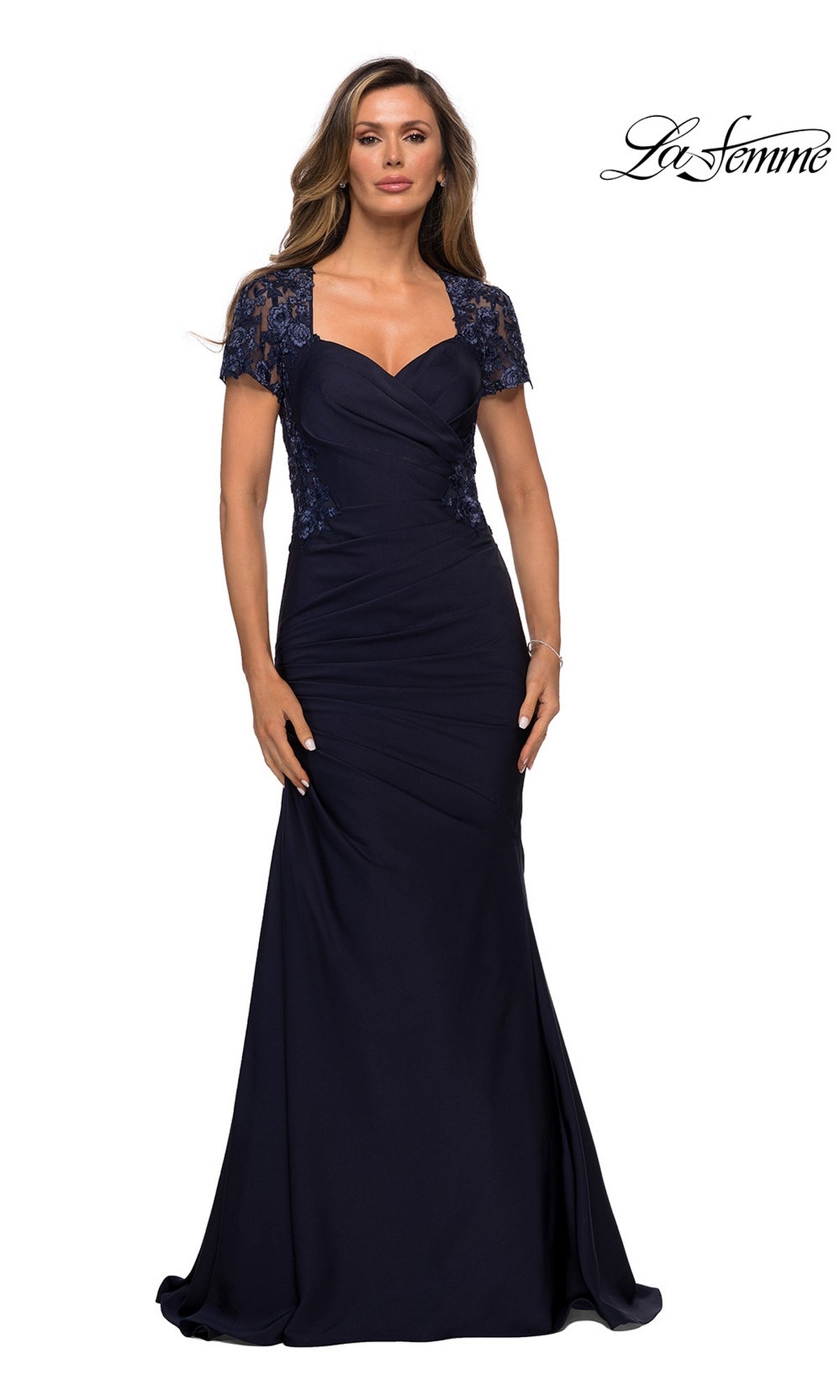 A woman stands against a white background wearing the La Femme 27989 long formal dress in navy, a floor-length evening gown with lace short sleeves, a ruched bodice, and delicate lace appliqué.