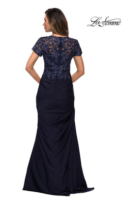 A woman wearing the La Femme 27989 long formal dress in floor-length navy satin-jersey, featuring lace detailing, elegant lace applique on the back, and short sleeves, stands with her back to the camera.