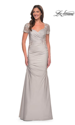 A woman stands smiling in the Long Formal Dress: La Femme 27989, a silver floor-length gown crafted from satin-jersey with short lace sleeves and gathered detailing, posing against a white background. Delicate lace appliqué enhances the elegance of this sophisticated dress. The “La Femme” logo is displayed in the top right corner.