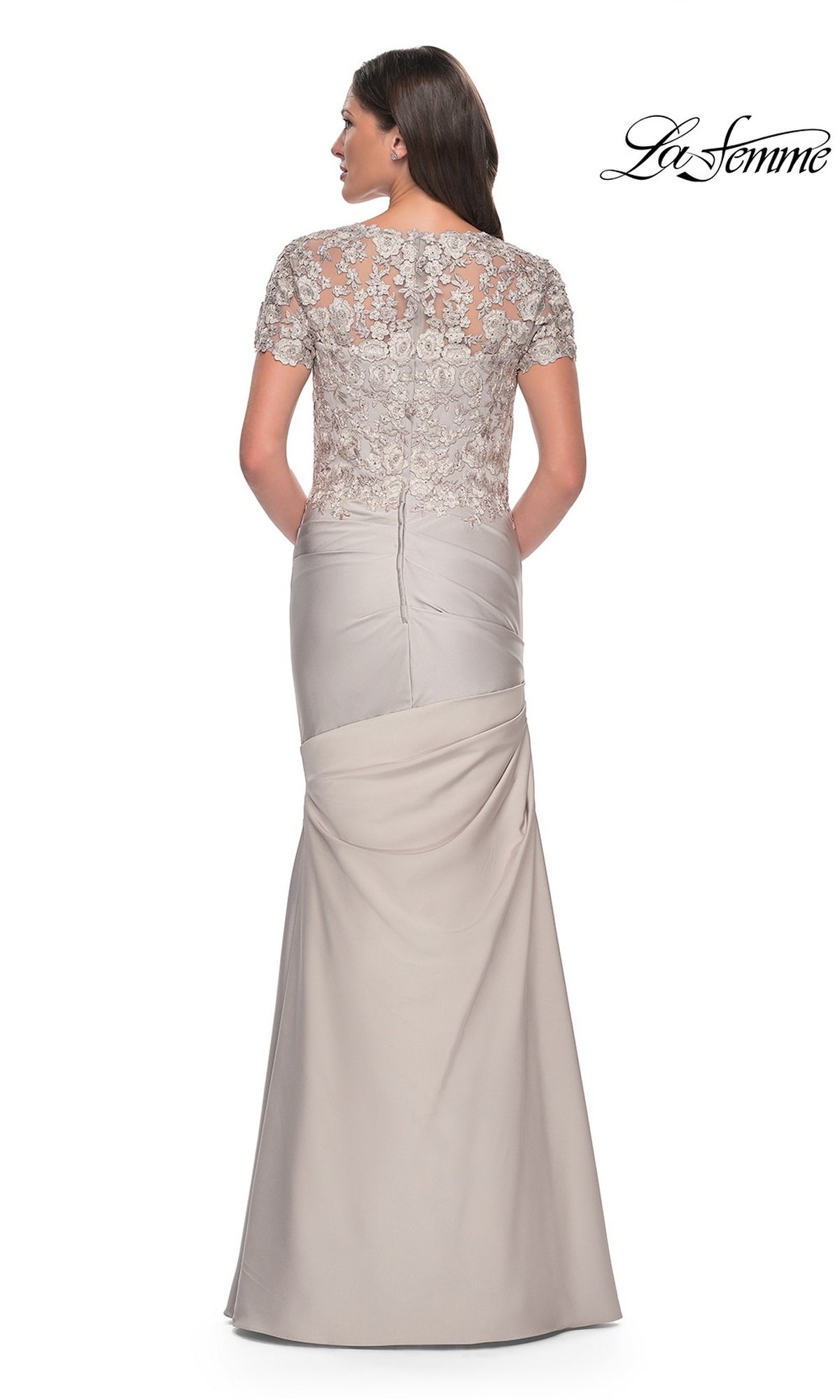 A woman faces away from the camera wearing the Long Formal Dress: La Femme 27989, which features a long, light gray satin-jersey design with a fitted trumpet silhouette skirt and a lace applique short-sleeved bodice. The “La Femme” logo is visible in the top right corner.