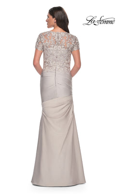 A woman faces away from the camera wearing the Long Formal Dress: La Femme 27989, which features a long, light gray satin-jersey design with a fitted trumpet silhouette skirt and a lace applique short-sleeved bodice. The “La Femme” logo is visible in the top right corner.
